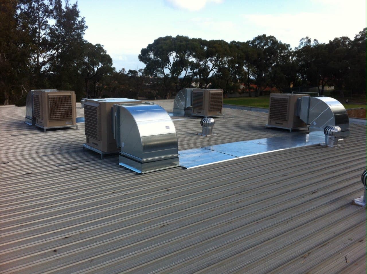 Four commercial Bonaire evaporative units with sheet metal ducting transitions on a large colorbond roof