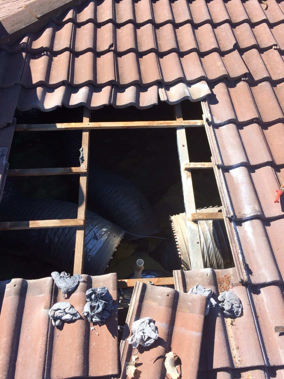 Roof tiles lifted to expose insulated flexible ducting being run through the roof cavity